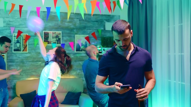 Bebaarde jonge vrouw met een bierflesje tijdens het browsen verveeld op smartphone op het feest.