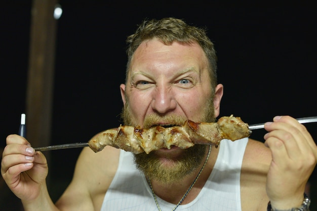 Bebaarde man eet heerlijke barbecue. een man met een rode baard eet spiesjes van spiesjes.