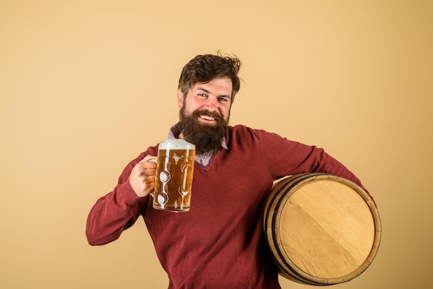 Foto bebaarde man houdt glas en vat vast met ambachtelijk bier aantrekkelijke bebaarde brouwer met houten vat van