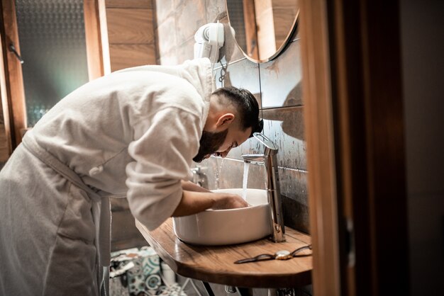 Bebaarde man in een badjas in de badkamer. Bruidegomochtend bereidt zich voor op bruiloft in het hotel. Mode foto van een man.