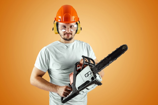 Bebaarde man in een helm heeft een kettingzaag op een oranje achtergrond