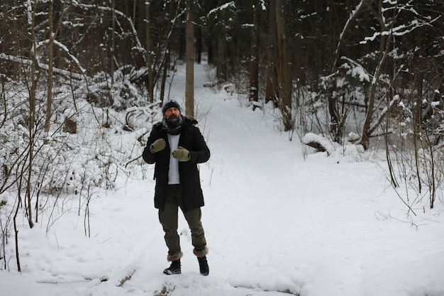 Bebaarde man in het winterbos. Aantrekkelijke gelukkige jonge man met baard lopen in het park.