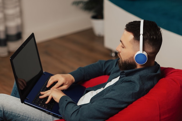 Bebaarde man in koptelefoon luisteren muziek en kijken op het scherm van de laptop thuis. Leeg scherm