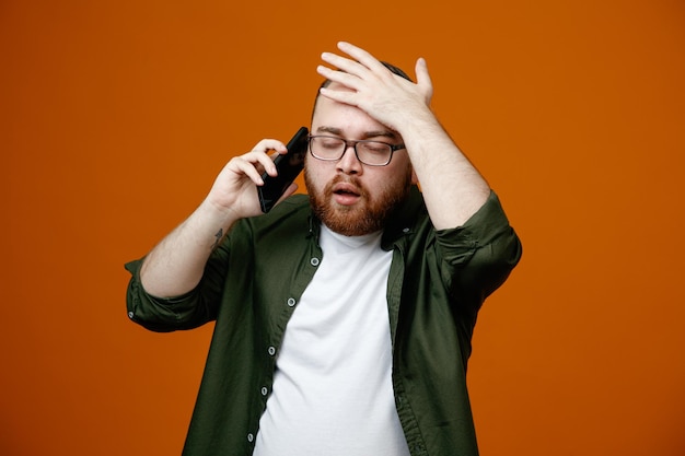 Foto bebaarde man in vrijetijdskleding met een bril die verward kijkt terwijl hij op een mobiele telefoon praat en de hand op zijn hoofd houdt voor een fout die over een oranje achtergrond staat