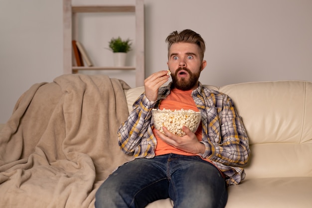 Bebaarde man kijken naar film of sport games Tv popcorn eten in huis 's nachts. Bioscoop-, kampioenschaps- en vrijetijdsconcept.