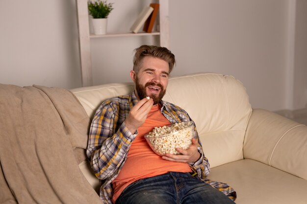 Bebaarde man kijken naar film of sport games Tv popcorn eten in huis 's nachts.