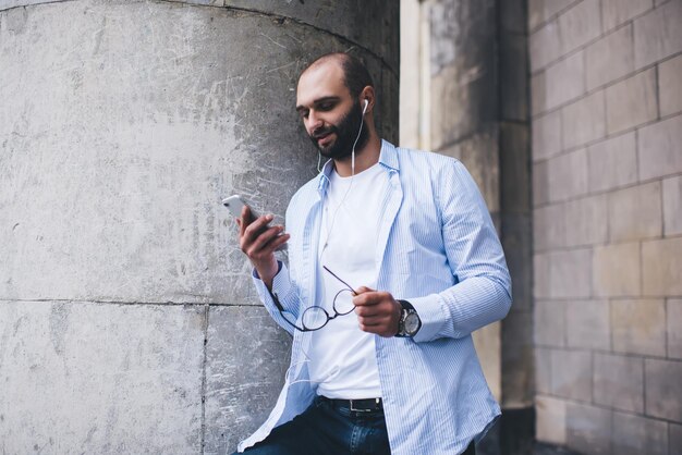 Bebaarde man kijken naar smartphone met koptelefoon buitenshuis