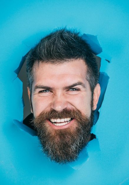 Bebaarde man kijkt door blauw papier weergave van mannelijk gezicht door papier lachende bebaarde man maken