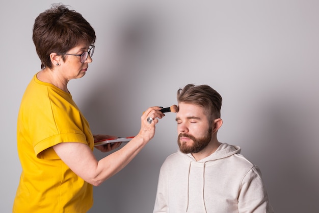 Bebaarde man krijgt make-up vrouw visagist werkt met borstel