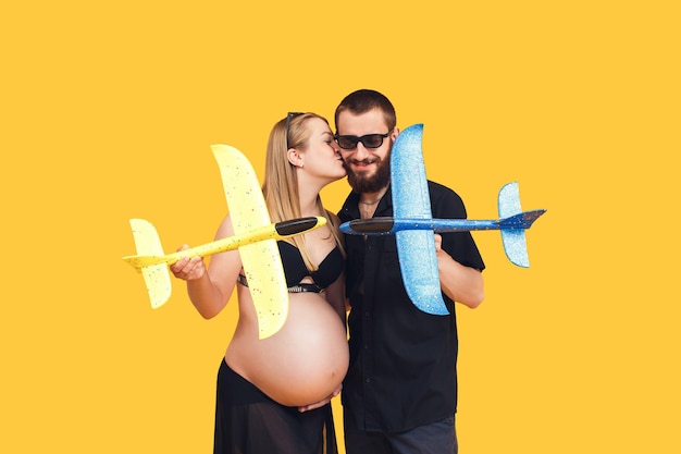 Bebaarde man kust een zwanger meisje op een gele achtergrond Paar spelen met vliegtuigen vreedzame hemel concept bescherming tegen luchtaanval