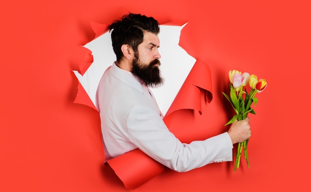 Bebaarde man met een boeket bloemen kijkend door een papieren gat zakenman met een boeket tulpen