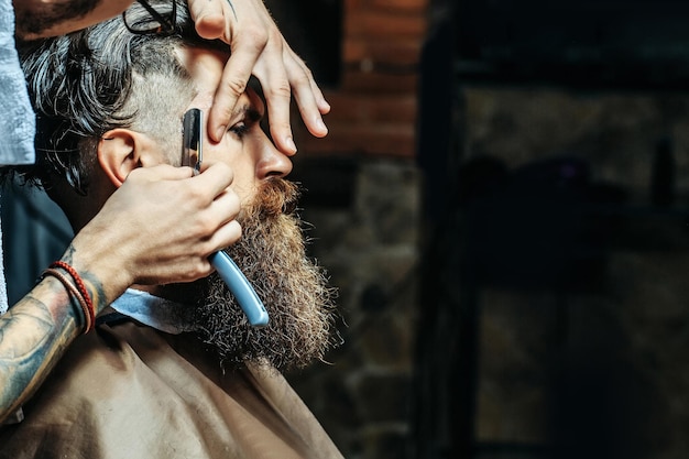 Bebaarde man met lange baard die haar scheert met scheermes