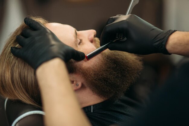 Bebaarde man met lange baard krijgt stijlvol haar scheerkapsel met scheermes door kapper in kapperszaak