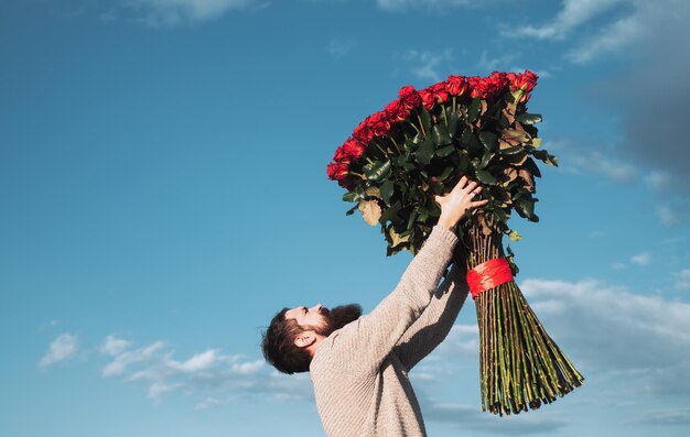 Bebaarde man met rode roos boeket Valentijnsdag cadeau met liefde knappe man op achtergrond hemel cadeau