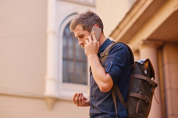 Bebaarde man met rugzak spreken via smartphone in een oude Europese stad.