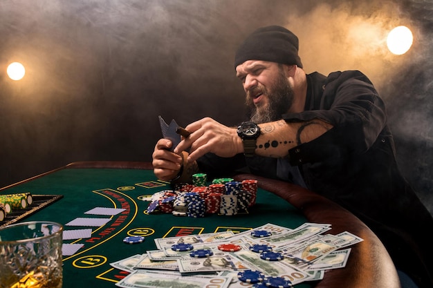 Bebaarde man met sigaar en glas zitten aan de pokertafel in een casino. Gokken, kaarten en roulette.