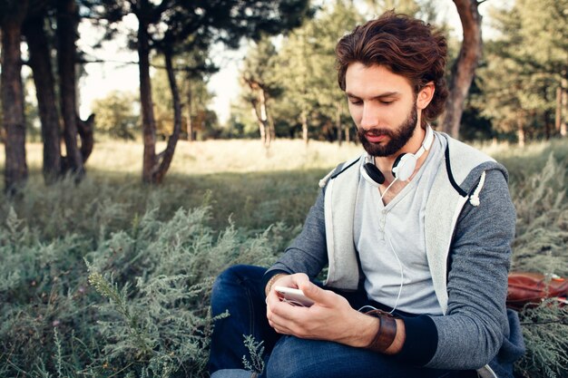 Bebaarde man met smartphone zittend in het bos.