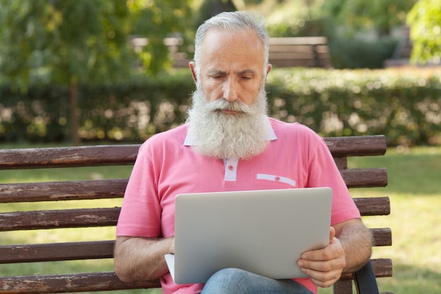 Bebaarde man op een bankje met behulp van een laptop