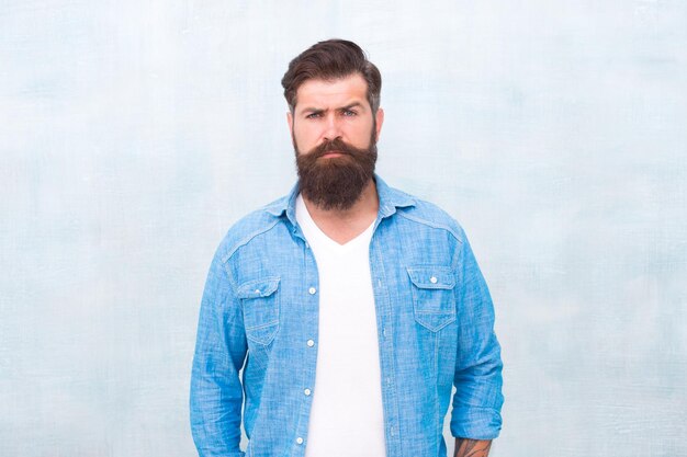 Bebaarde man trendy hipster stijl mannelijkheid en mannelijke schoonheid concept Hipster met baard en snor dragen denim shirt goed verzorgde macho brutale knappe hipster man op grijze muur achtergrond