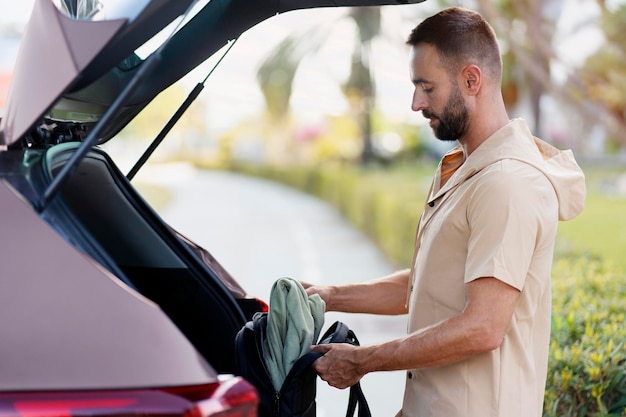 Bebaarde man van middelbare leeftijd die zak in autokoffer laadt, transportconcept