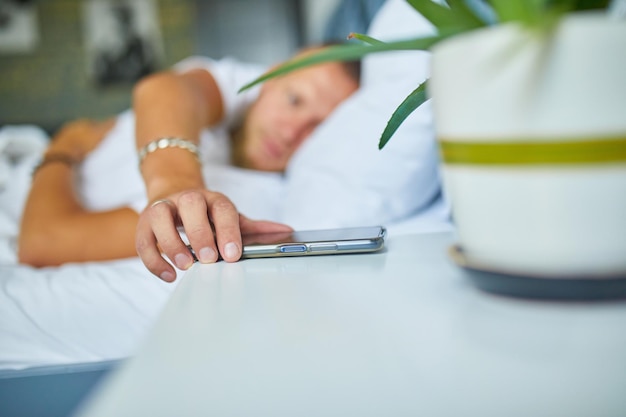 Bebaarde man wakker op een groot en gezellig bed met mobiele wekker gewekt door