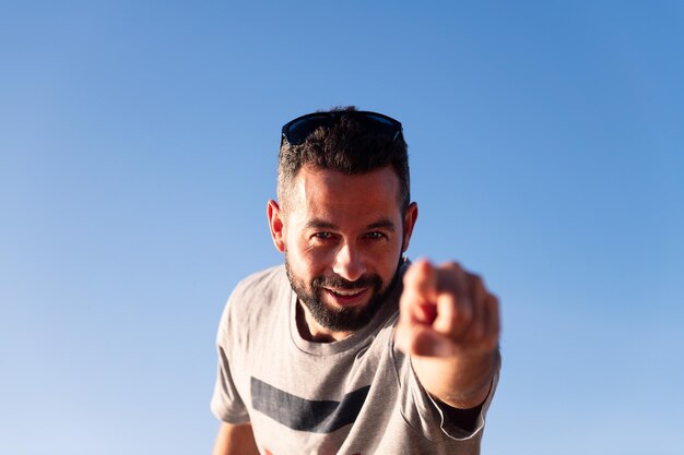 Bebaarde man wijzende vinger naar camera met blauwe lucht in achtergrond kopie ruimte voor tekst