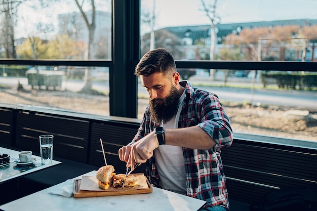 Bebaarde man zit in een restaurant en eet een verse smakelijke burger