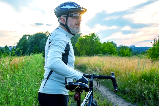 Bebaarde mannelijke fietser rust met een fiets op de weg in natuurfietsen en gezondheidshobby's