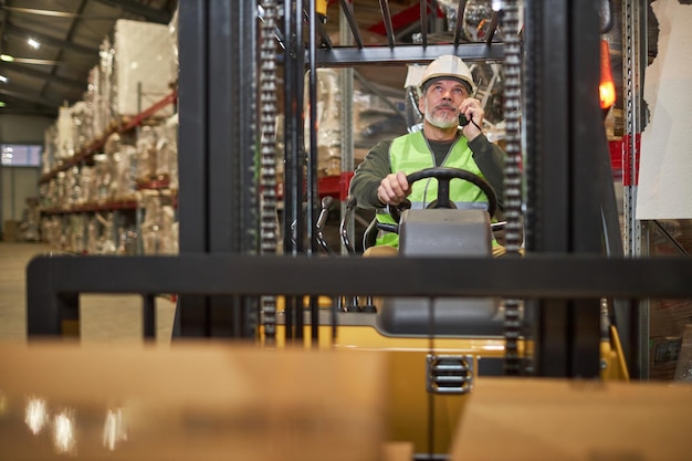 Bebaarde mannelijke werknemer vorkheftruck rijden in magazijn