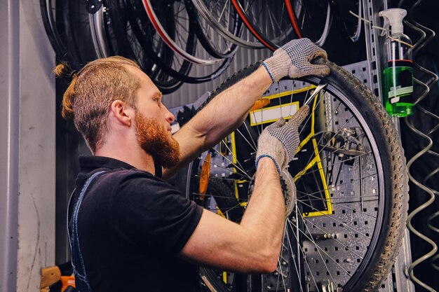 Bebaarde monteur die fietswielband in een werkplaats repareert. Achteraanzicht, servicehandleiding.