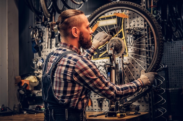Bebaarde monteur doet fietswiel servicehandleiding in een werkplaats.