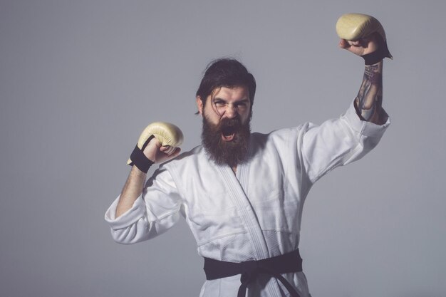 Bebaarde schreeuwende gelukkige karate man in kimono en bokshandschoenen