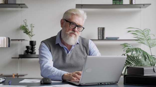 Bebaarde senior man aan het werk met laptop in kantoor