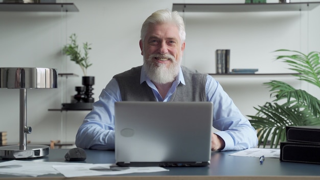 Bebaarde senior man aan het werk met laptop in kantoor