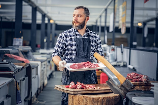 Bebaarde slager gekleed in een fleece-shirt die vers gesneden vlees serveert op een markt.