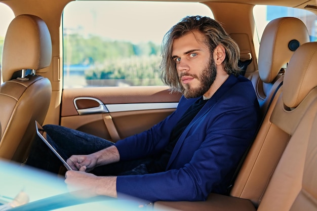 Bebaarde stijlvolle man zit in een auto en werkt met papieren documenten.