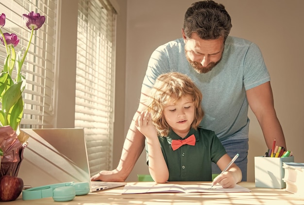 Foto bebaarde vader die schoolhuiswerk schrijft met zijn zoontje in het ouderschap in de klas