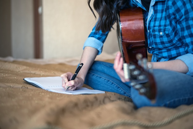 Bebouwd beeld van vrouwelijke handen die in een notitieboekje met een akoestische gitaar schrijven