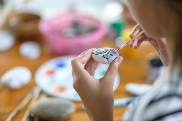 Bebouwd schot van het jonge meisjeskunstenaar schilderen met waterkleur op rots.