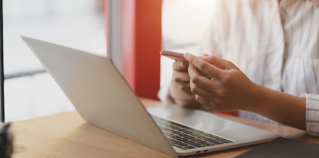 Bebouwd schot van jonge smartphone van de onderneemsterholding terwijl het werken aan laptop computer