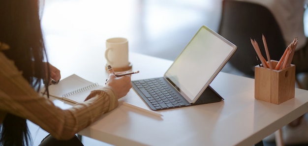 Bebouwd schot van jonge vrouwelijke ontwerper die haar project met digitale tablet in modern bureau opstellen