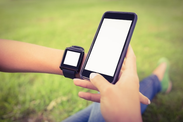 Bebouwde handen van persoon die slim horloge dragen en smartphone houden bij park