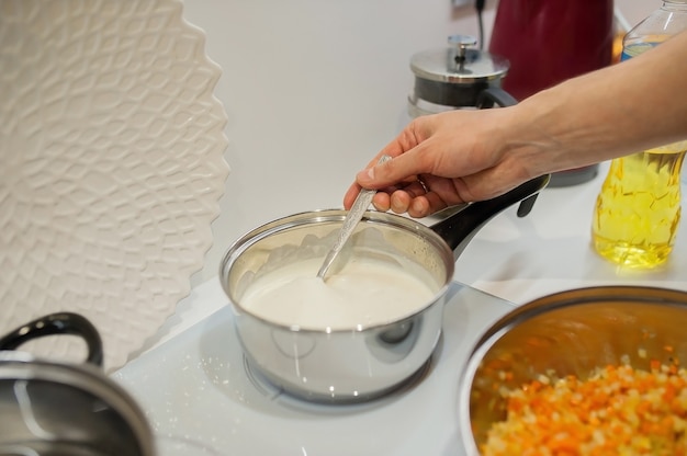 Foto bechamelsaus op inductie kookplaat kookroer met lepel. we blijven thuis en koken lasagnin in de keuken.