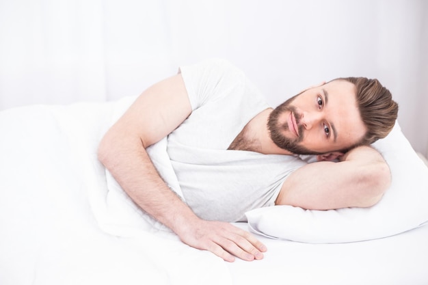 Bed- en rusttijd Vermoeide millennial knappe bebaarde man in slaap vredig rustend in wit comfortabel bed in slaapkamer kopie ruimte Ontspan slaapdutje thuis in het weekend