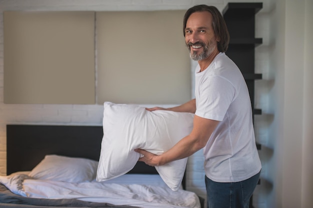 Bed opmaken. Bebaarde volwassen man die 's ochtends zijn bed opmaakt