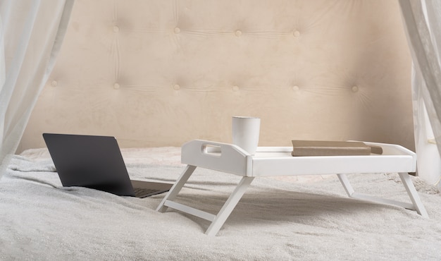 Bed serving table and a laptop on bed. Freelancer workplace concept, Notebook computer and cup of coffee