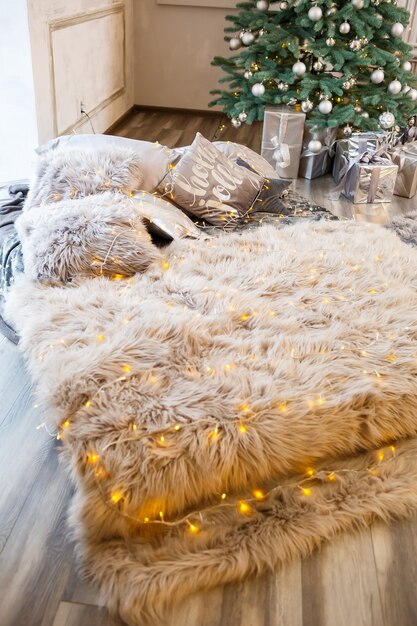 The bed with New Year's decor stands against the background of a decorated Christmas tree. Festive decoration in the house with yellow garlands