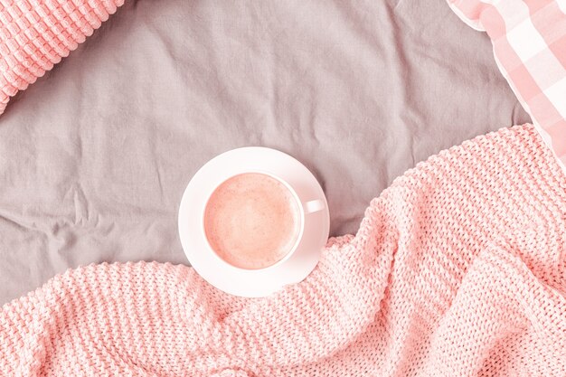 Bed with pink knitted plaid and coffee, top view, copy space, flat lay.