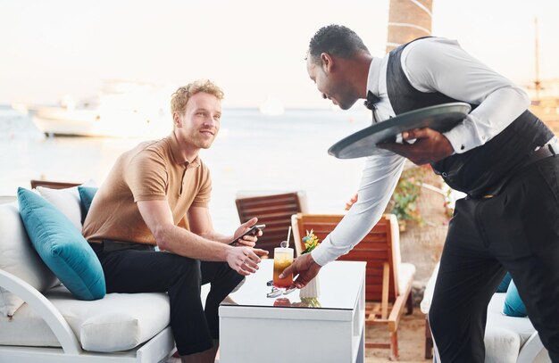 Bediend door ober Jonge man is buiten op zonnige dag Concept van vakantie