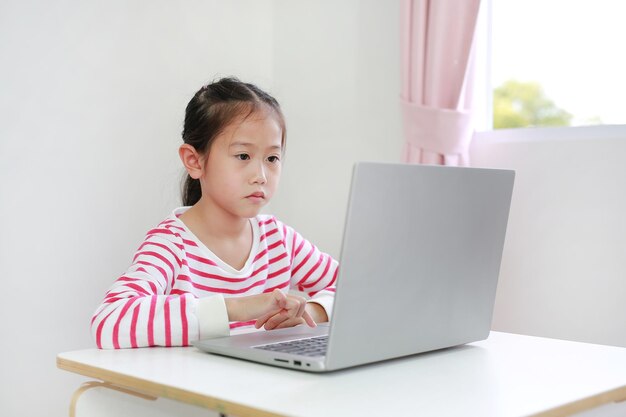 Bedoel een Aziatisch klein kind dat aan een bureau zit en thuis een laptop gebruikt